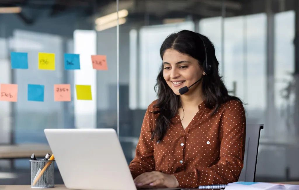 Call handler wearing a headset answering customer calls at a laptop in an office